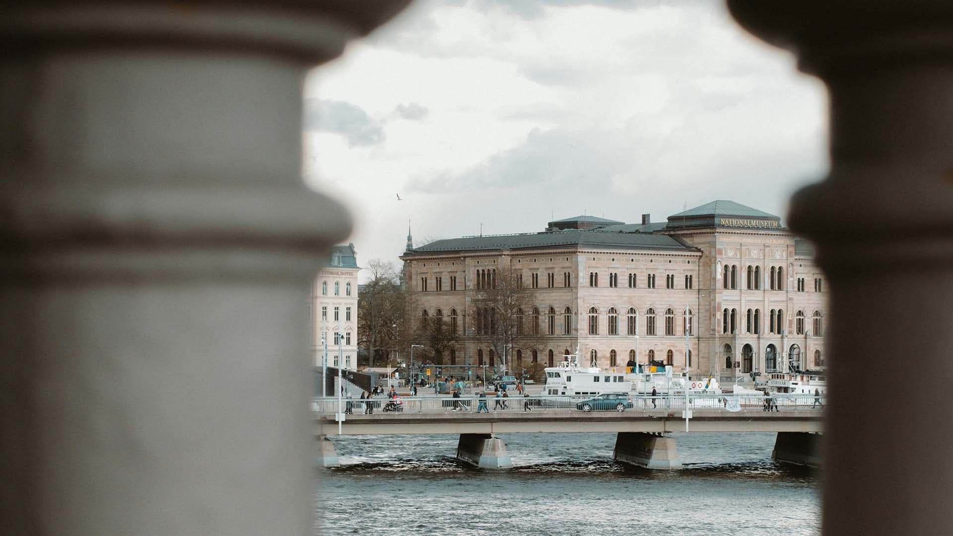 Historisk byggnad vid vattnet i centrala Stockholm, sedd mellan två pelare.