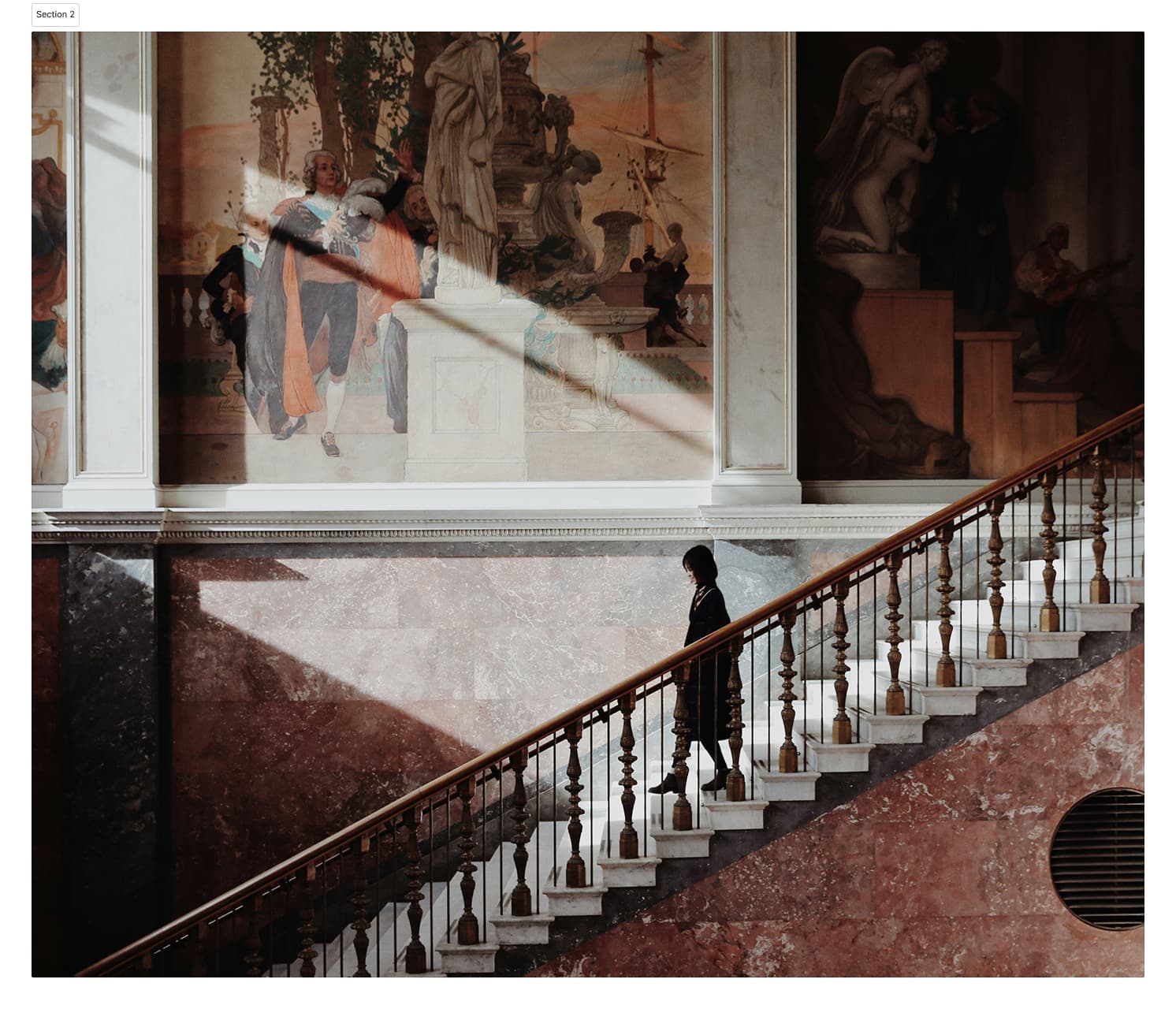 A woman walks down a staircase in a beautifully decorated historic building.
