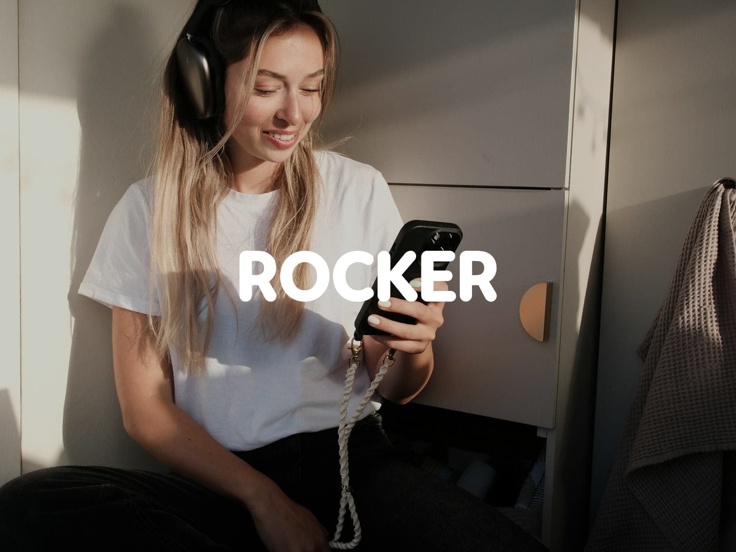 Young woman wearing headphones smiling at her phone, with the Rocker logo in white overlaid on the image.